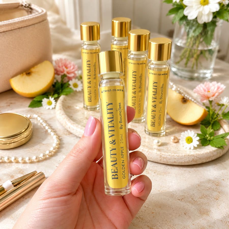 A hand holding a gold Boundless golden apple twist-to-mix shot, with more vials and fresh apples behind